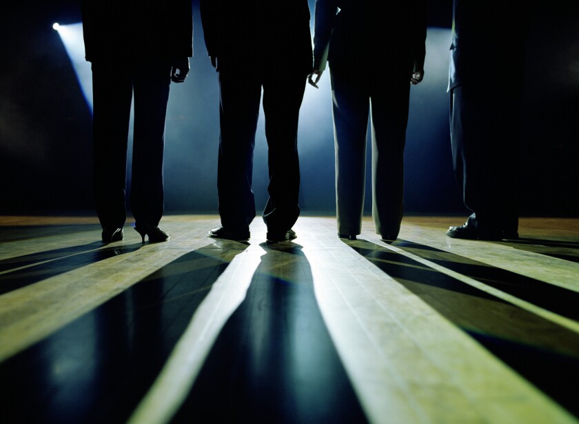 Business executives standing on stage facing spotlight, rear view