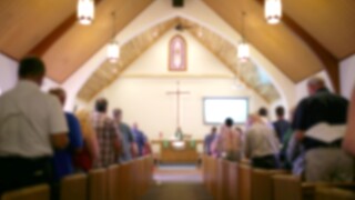Blurred Photo of the Iterior of a Church Sanctuary with Congregation, Pastor, and a Large Cross Visible