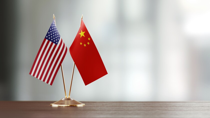 American And Chinese Flag Pair On A Desk Over Defocused Background