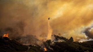Water is dropped on the advancing Palisades Fire by helicopter in the Pacific Palisades neighborhood of Los Angeles, Tuesday, Jan. 7, 2025. (AP Photo/Ethan Swope)