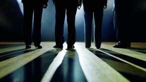 Business executives standing on stage facing spotlight, rear view